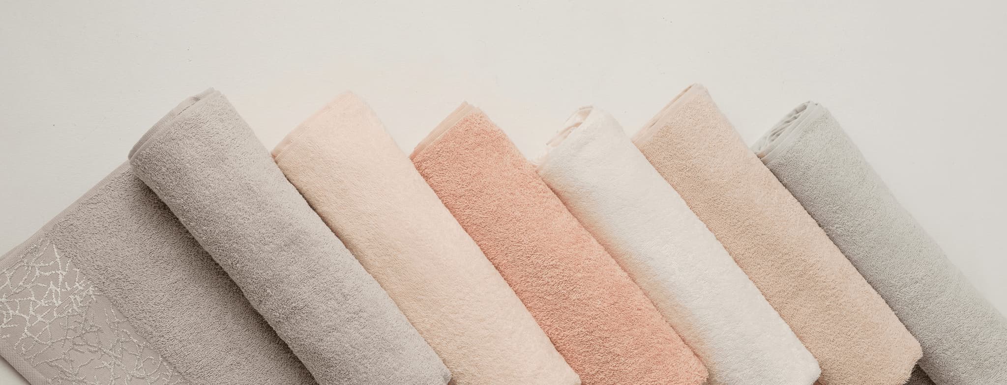 Stack of soft pastel towels in gray, blush pink, peach and white tones on a neutral background