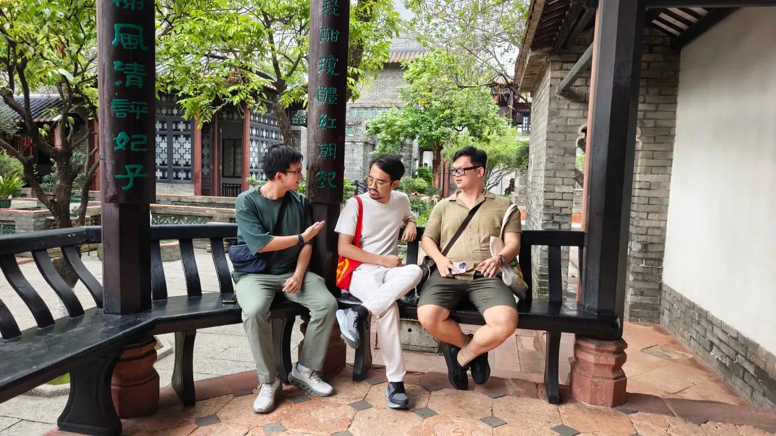 Students sitting and chatting on a bench at a campus courtyard under green trees