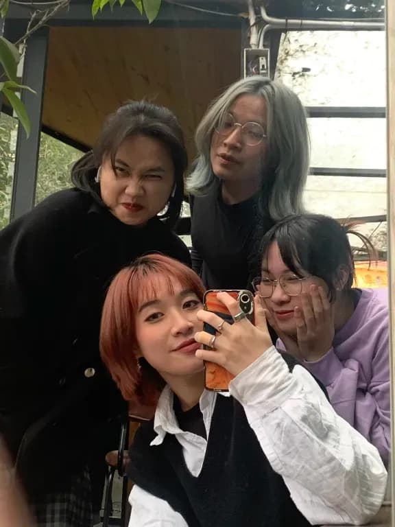 Group selfie of five friends with colorful hair in a cozy indoor setting by a window