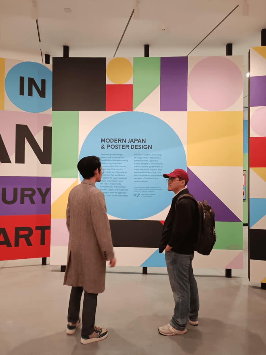 People viewing Modern Japan & Poster Design exhibition wall with colorful geometric poster panels at art gallery