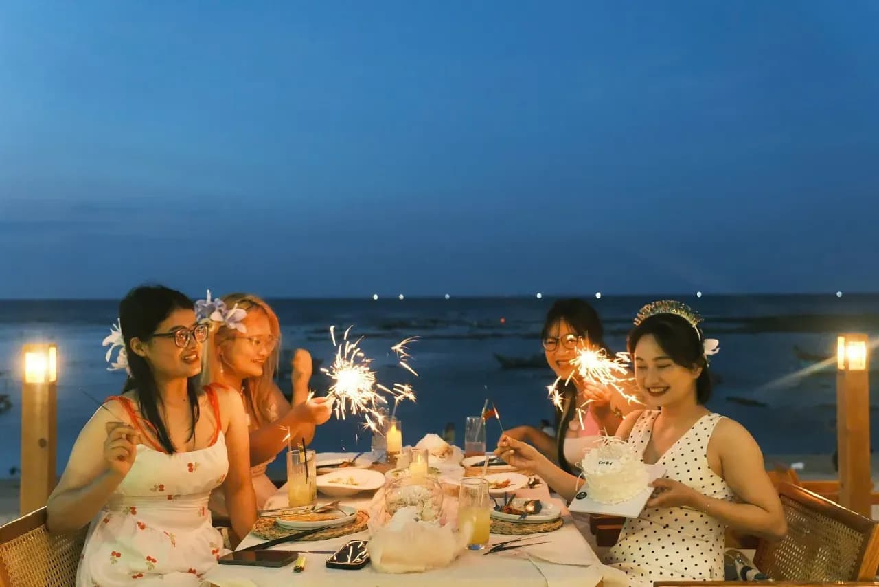 Friends celebrating a birthday dinner on a seaside terrace with sparklers at dusk, outdoor party celebration