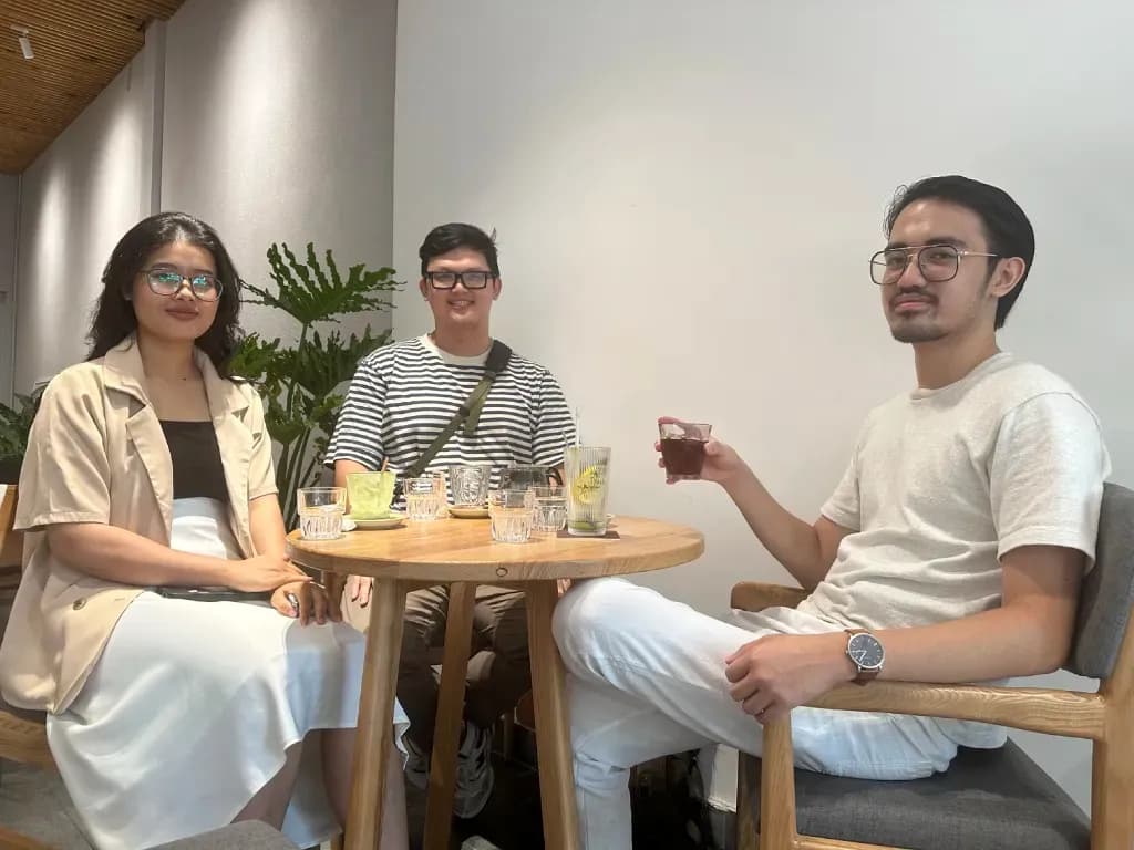 Three people chatting at a café table with drinks and desserts, indoor casual setting