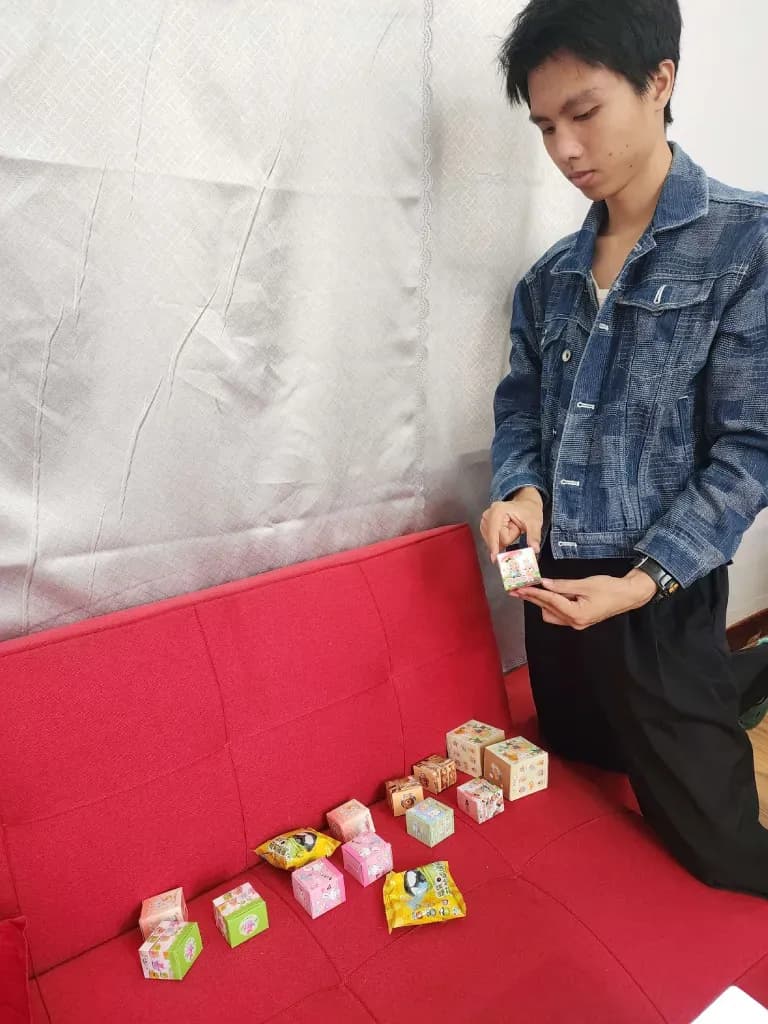 Young man arranging small boxed treats on a red booth display at an event or shop table