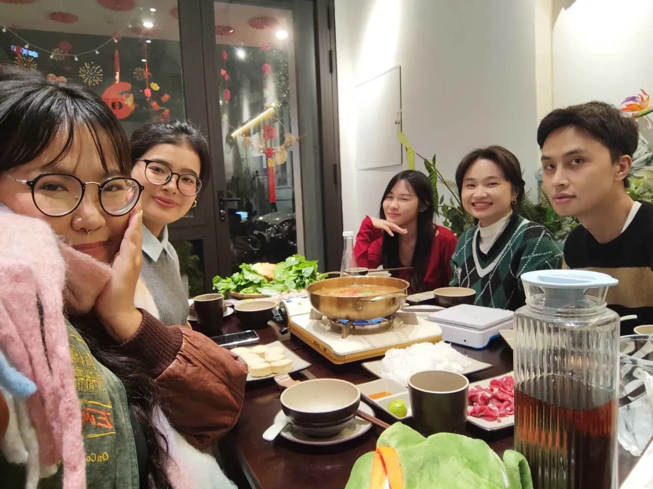 Friends enjoying Korean BBQ dinner at a restaurant, sharing a hot pot meal with drinks and side dishes