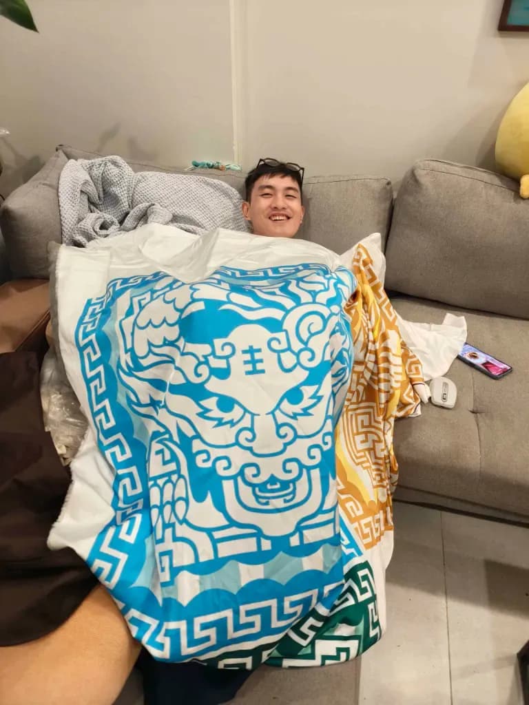 Smiling man relaxing on a sofa wrapped in a blue patterned blanket with golden design accents