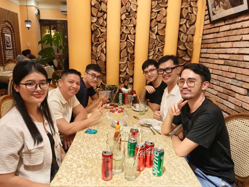 Group of friends celebrating at restaurant table with drinks and birthday cake, Vietnamese diners at party