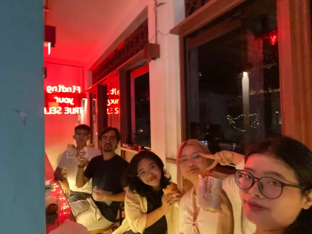 Friends dining in a warmly lit restaurant with red neon lighting and string lights, group celebration night out