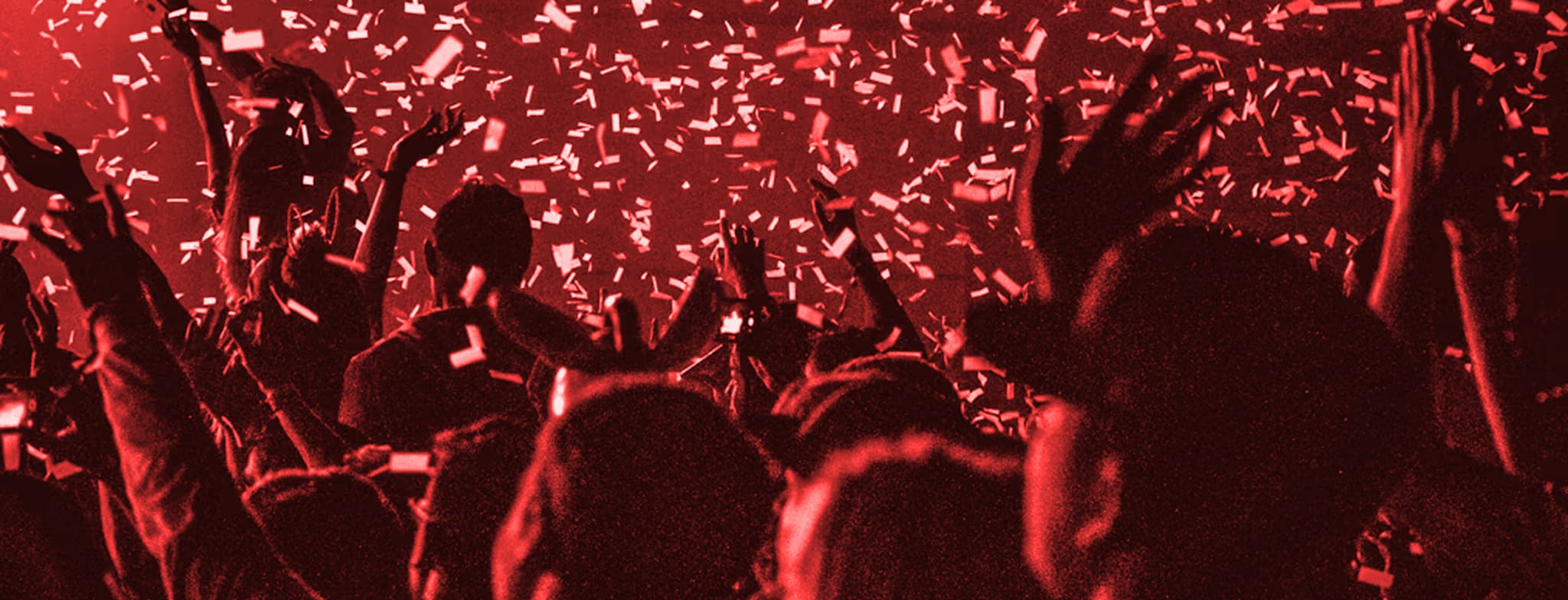 Crowd celebrating at a red-lit concert with raised hands and falling confetti
