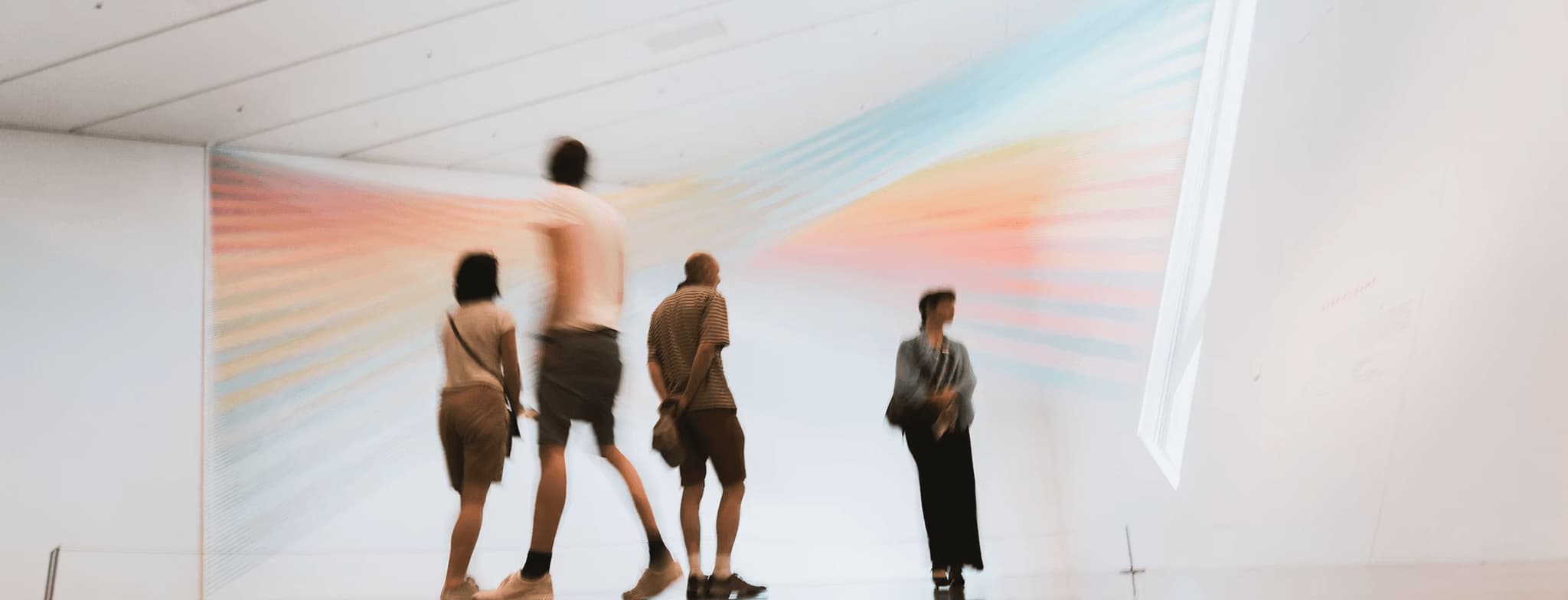 Four people view a colorful abstract wall projection in a contemporary art gallery installation.