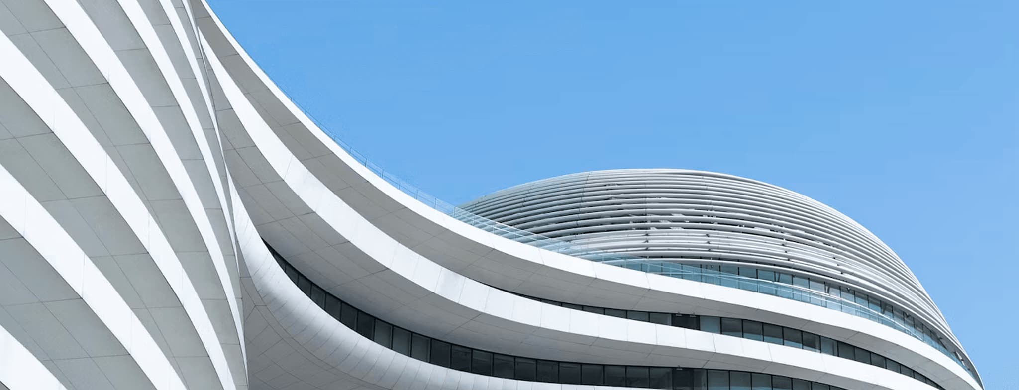 Modern curved white building facade with horizontal glass windows under a clear blue sky