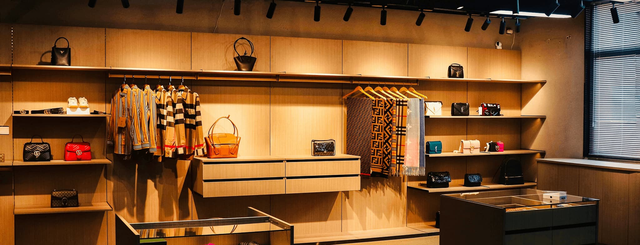 Warmly lit fashion boutique interior with clothing racks, handbags, shelves, and display counters