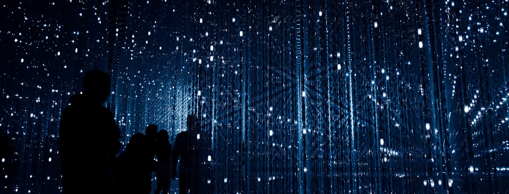 Visitors silhouetted in immersive blue LED light installation with sparkling digital patterns